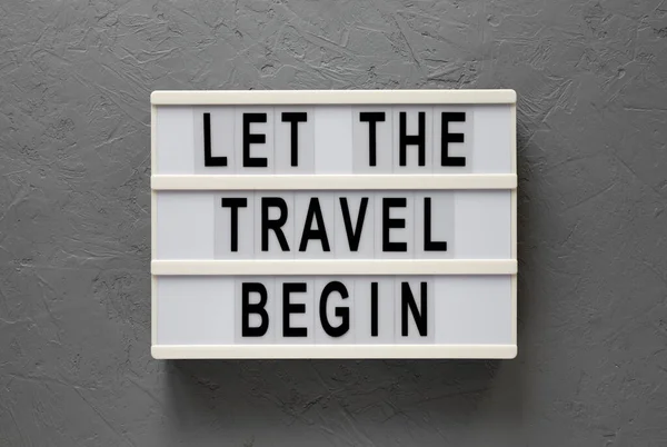 \'Let the travel begin\' on a lightbox on a gray background, top view. Flat lay, from above, overhead.