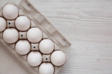 Beyaz ahşap bir yüzey üzerinde, kağıt bir kutuda pişmemiş organik beyaz yumurtalar. Dümdüz, tepeden, yukarıdan. Boşluğu kopyala.