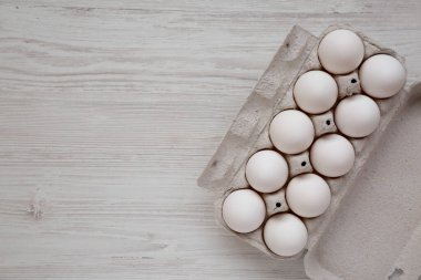 Beyaz ahşap bir yüzey üzerinde, kağıt bir kutuda pişmemiş organik beyaz yumurtalar. Dümdüz, tepeden, yukarıdan. Boşluğu kopyala.