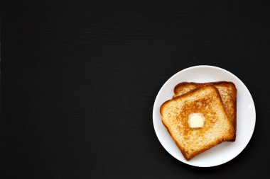 Siyah arka planda beyaz bir tabakta ev yapımı tereyağlı tost. Dümdüz, tepeden, yukarıdan. Boşluğu kopyala.