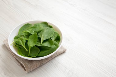 Beyaz ahşap arka planda beyaz bir kasede taze ıspanak, yan görüş. Boşluğu kopyala.