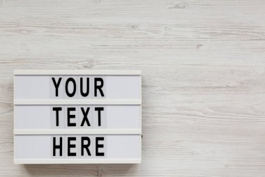 'Buradaki metnin' beyaz ahşap bir yüzey üzerindeki ışık kutusunda, üst görünümde. Dümdüz, tepede. Boşluğu kopyala.