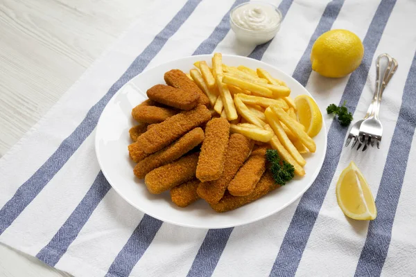 Homemade Fish Sticks and French Fries with Tartar Sauce on a white wooden background, low angle view.