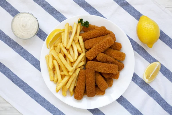 Homemade Fish Sticks and Fries with Tartar Sauce on a white wooden table, top view. Flat lay, overhead, from above.