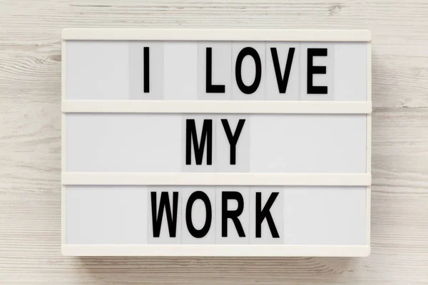 'I love my work' on a lightbox on a white wooden background, top view. Flat lay, from above, overhead.