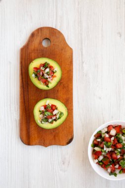 Ev yapımı Pico de Gallo Doldurulmuş Avokado beyaz ahşap arka planda, ahşap bir tahta üzerinde, üst manzara. Dümdüz, tepeden, yukarıdan. Boşluğu kopyala.