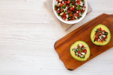 Ev yapımı Pico de Gallo Doldurulmuş Avokado beyaz ahşap arka planda, ahşap bir tahta üzerinde, üst manzara. Dümdüz, tepeden, yukarıdan. Metin için boşluk.