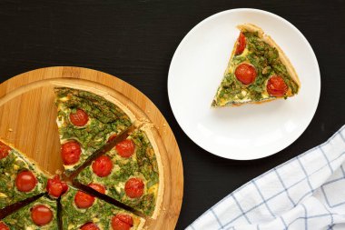 Siyah arka planda beyaz bir tabakta ev yapımı ıspanaklı kiş. Dümdüz, tepeden, yukarıdan. 