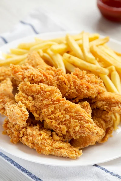 Homemade Crispy Chicken Tenders and French Fries on a white plate, side view. Close-up.