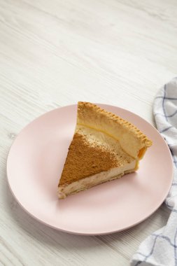 Beyaz ahşap bir masada pembe bir tabakta ev yapımı şekerli kremalı turta. Düşük açılı. Boşluğu kopyala. 