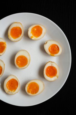 Ev yapımı Unami Soya Sosu Yumurtası, beyaz tabakta, siyah bir yüzey üzerinde, üst manzara. Yukarıdan, dümdüz uzanmış.