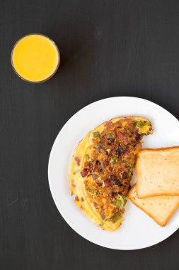 Siyah bir yüzey üzerinde beyaz bir tabakta ev yapımı Denver omleti, üst manzara. Dümdüz, tepeden, yukarıdan.