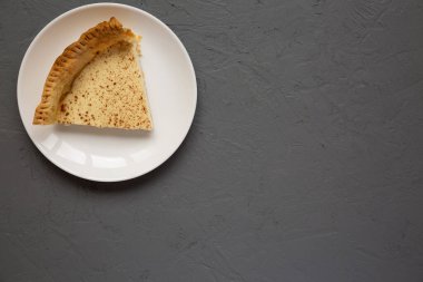 Ev yapımı kremalı turta, beyaz bir tabakta, gri arka planda, üst tarafta. Dümdüz, tepeden, yukarıdan. Boşluğu kopyala.