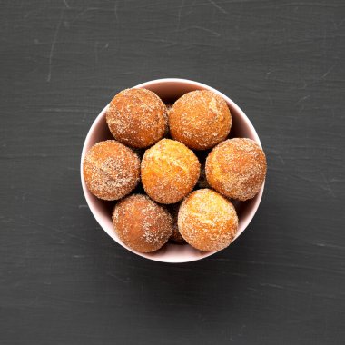 Siyah bir yüzey üzerinde pembe bir kasede ev yapımı kızarmış çörek delikleri, üst manzara. Dümdüz, tepeden, yukarıdan.