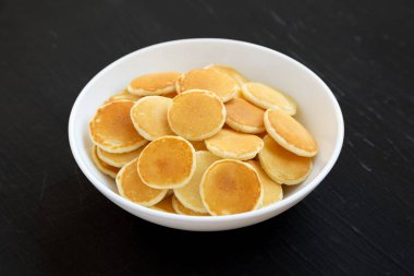 Siyah bir yüzey üzerinde beyaz bir kâsede ev yapımı Mini Krep Gevreği..