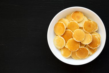 Siyah bir yüzey üzerinde beyaz bir kâsede ev yapımı Mini Krep Gevreği. Dümdüz, tepeden, yukarıdan. Metin için boşluk.