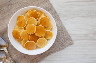 Beyaz ahşap bir yüzey üzerinde beyaz bir kâse içinde ev yapımı Mini Krep Gevreği. Dümdüz, tepeden, yukarıdan. Boşluğu kopyala.