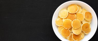 Siyah arka planda beyaz bir kasede ev yapımı Mini Krep Gevreği. Dümdüz, tepeden, yukarıdan. Metin için boşluk.