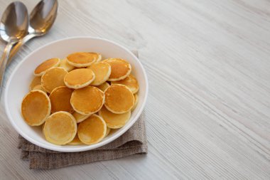 Beyaz ahşap bir masada beyaz bir kâse içinde ev yapımı Mini Krep Gevreği, yan görüş. Metin için boşluk.
