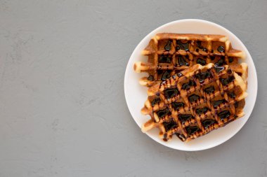 Gri bir yüzey üzerinde beyaz bir tabakta nefis ev yapımı Belçika şekerli waffle 'ları. Dümdüz, tepeden, yukarıdan. Boşluğu kopyala.