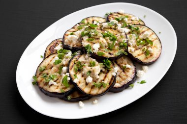 Siyah arka planda beyaz bir tabakta Feta ve şifalı otlu ev yapımı ızgara patlıcan..