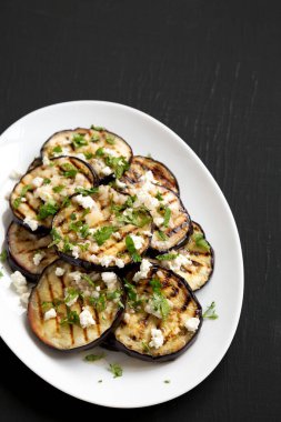 Siyah arka planda beyaz tabakta Feta ve şifalı otlu ev yapımı ızgara patlıcan. Boşluğu kopyala.