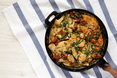 Beyaz ahşap bir masada dökme demir bir tavada ev yapımı kremalı Toskana tavuğu. Dümdüz, tepeden, yukarıdan. Boşluğu kopyala.