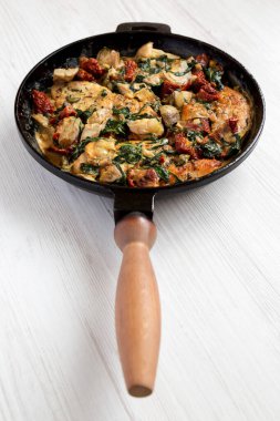 Beyaz ahşap arka planda dökme demir tavuklu ev yapımı kremalı Toskana tavuğu. Düşük açılı.. 