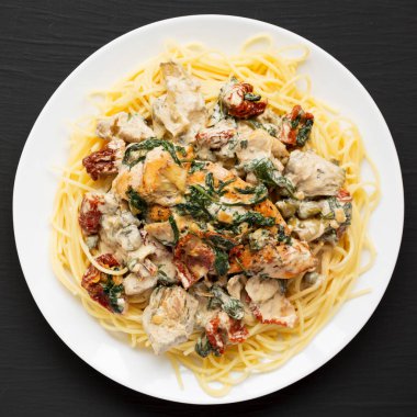 Siyah bir yüzey üzerinde beyaz bir tabakta makarna ile ev yapımı kremalı Toskana tavuğu. Dümdüz, tepeden, yukarıdan. Boşluğu kopyala.