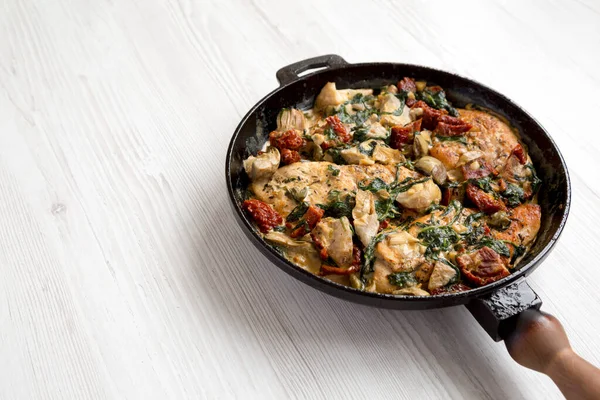 Beyaz ahşap yüzeyde dökme demir tavada ev yapımı kremalı Toskana tavuğu. Düşük açılı. Metin için boşluk.