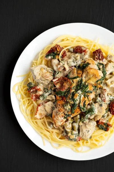 Siyah bir yüzey üzerinde beyaz bir tabakta makarna ile ev yapımı kremalı Toskana tavuğu. Dümdüz, tepeden, yukarıdan.