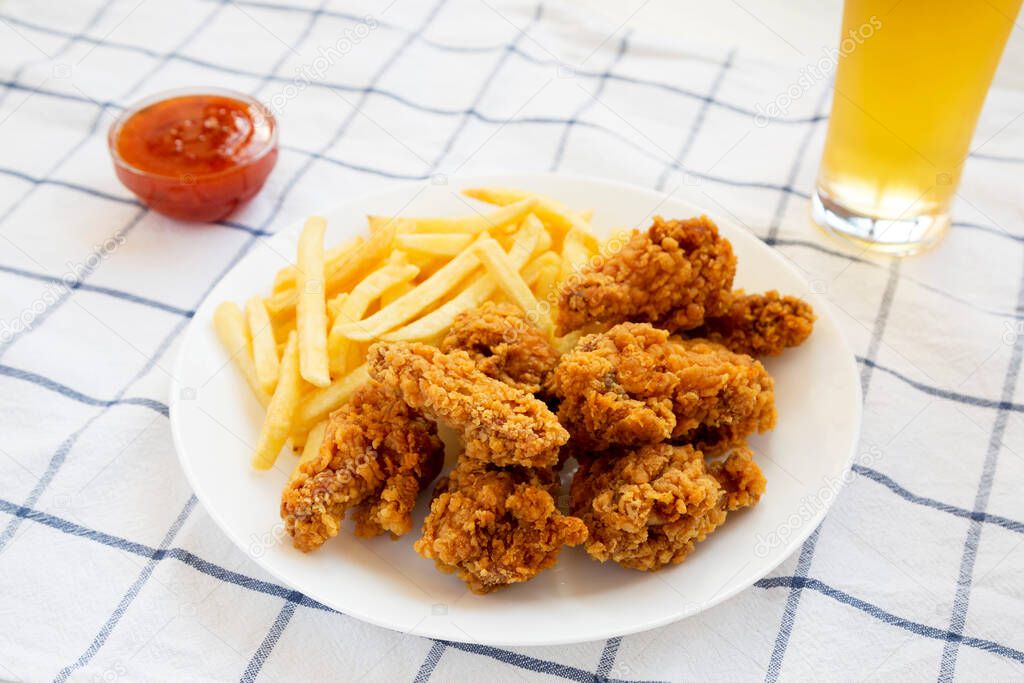 Homemade Crispy Chicken wings and French Fries with sour-sweet sauce and glass of cold beer on cloth, side view. 