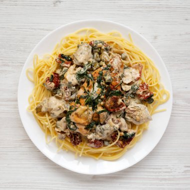 Beyaz ahşap bir yüzeyde beyaz bir tabakta makarna ile ev yapımı kremalı Toskana tavuğu.. 