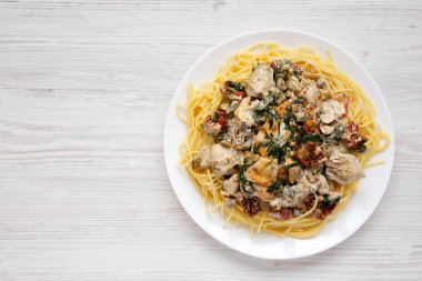 Beyaz ahşap arka planda beyaz bir tabakta makarna ile ev yapımı kremalı Toskana Tavuğu, üst manzara. Boşluğu kopyala.