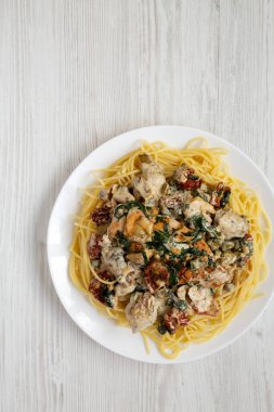 Beyaz ahşap arka planda beyaz bir tabakta makarna ile ev yapımı kremalı Toskana Tavuğu, üst manzara. Boşluğu kopyala.