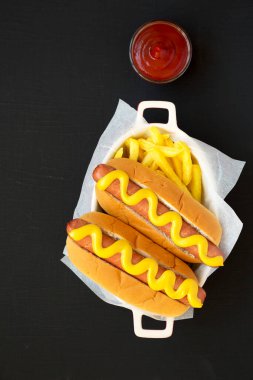 Siyah bir yüzey üzerinde patates kızartmalı ev yapımı hardal sosisli sandviç. Dümdüz, tepeden, yukarıdan.