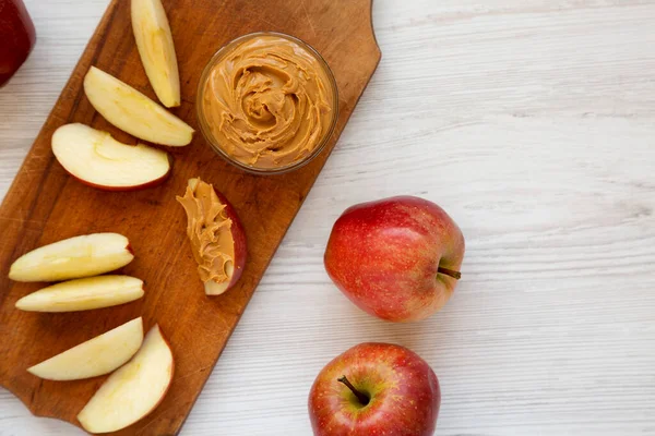 Raw Red Apples and Peanut Butter on a rustic wooden board on a white wooden table, top view. Copy space.