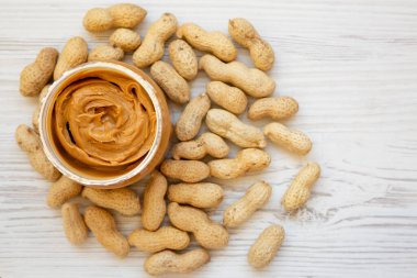 Beyaz ahşap arka planda fıstık ezmesi dolu kavanoz, üst manzara. Dümdüz, tepeden, yukarıdan. Boşluğu kopyala.