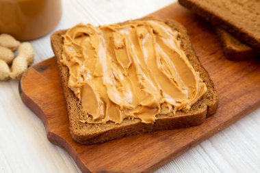 Beyaz ahşap arka planda, üzerinde Fıstık Ezmesi olan bir parça ekmek. Düşük açılı manzara.. 