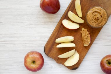Beyaz ahşap bir masanın üzerinde çiğ kırmızı elmalar ve fındık ezmesi, üst manzara. Metin için boşluk.