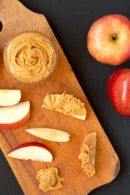 Kırmızı Elma ve Fıstık Ezmesi siyah arka planda, ahşap bir tahta üzerinde, üst manzara. Dümdüz, tepeden, yukarıdan. 