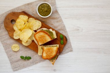Ev yapımı Pesto Tavuklu Sandviç, yanında patates cipsi, ahşap bir tahta üzerinde. Metin için boşluk.