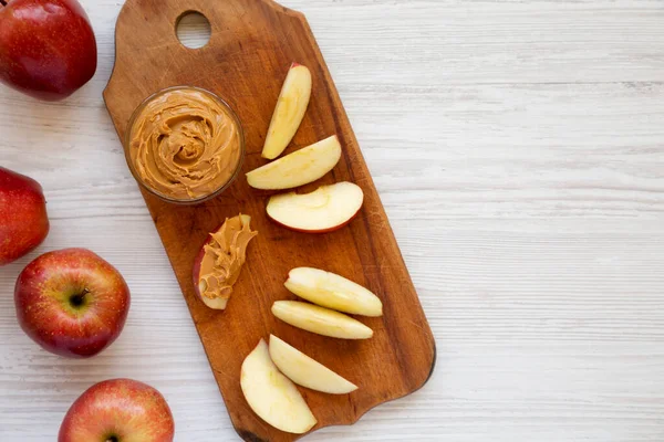 Raw Red Apples and Peanut Butter on a rustic wooden board on a white wooden surface, top view. Copy space.