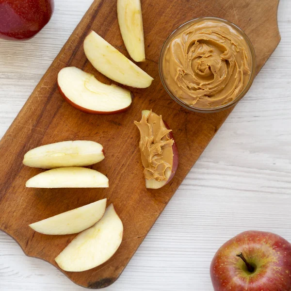 Raw Red Apples and Peanut Butter on a rustic wooden board on a white wooden background, top view. Flat lay, overhead, from above.