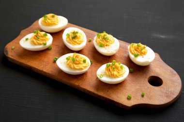 Siyah bir arka planda, ahşap bir tahtanın üzerinde Frenk soğanlı ev yapımı Deviled Eggs.. 