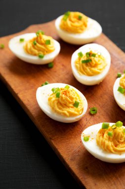 Siyah bir yüzey üzerinde ahşap bir tahtanın üzerinde soğanlı ev yapımı Deviled Eggs, yan görüş. Yakın plan..
