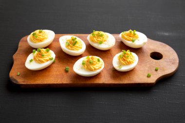 Siyah bir arka planda, ahşap bir tahtanın üzerinde Frenk soğanlı ev yapımı Deviled Eggs.. 