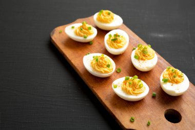 Siyah bir yüzey üzerinde ahşap bir tahtanın üzerinde soğanlı ev yapımı Deviled Eggs, yan görüş. Boşluğu kopyala.
