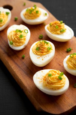 Siyah arka planda, ahşap bir tahtanın üzerinde soğanlı ev yapımı Deviled Eggs, yan görüş. Yakın plan..