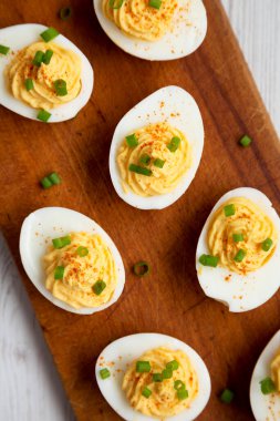 Beyaz ahşap arka planda, ahşap bir tahtanın üzerinde soğanlı ev yapımı Deviled Eggs, üst manzara. Dümdüz, tepeden, yukarıdan. 